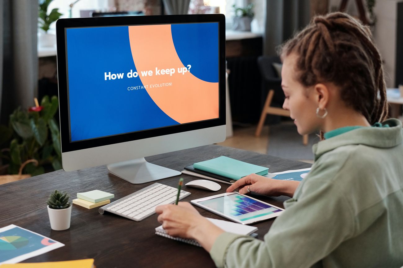 A woman working at a desktop computer showing the question How do we keep up?