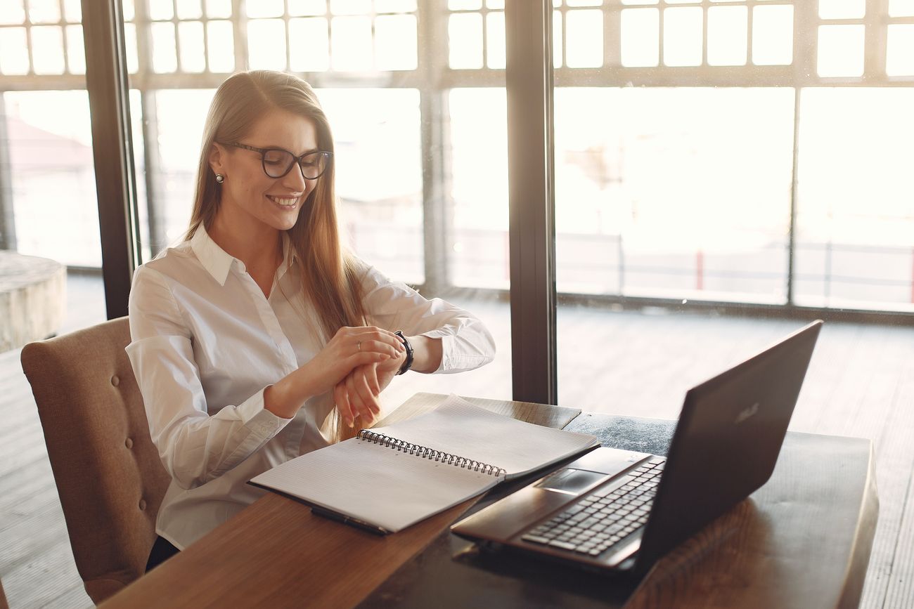A woman checking her watch while working at a laptop