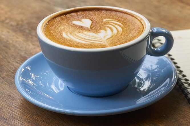 A latte in a blue cup beside an open notebook