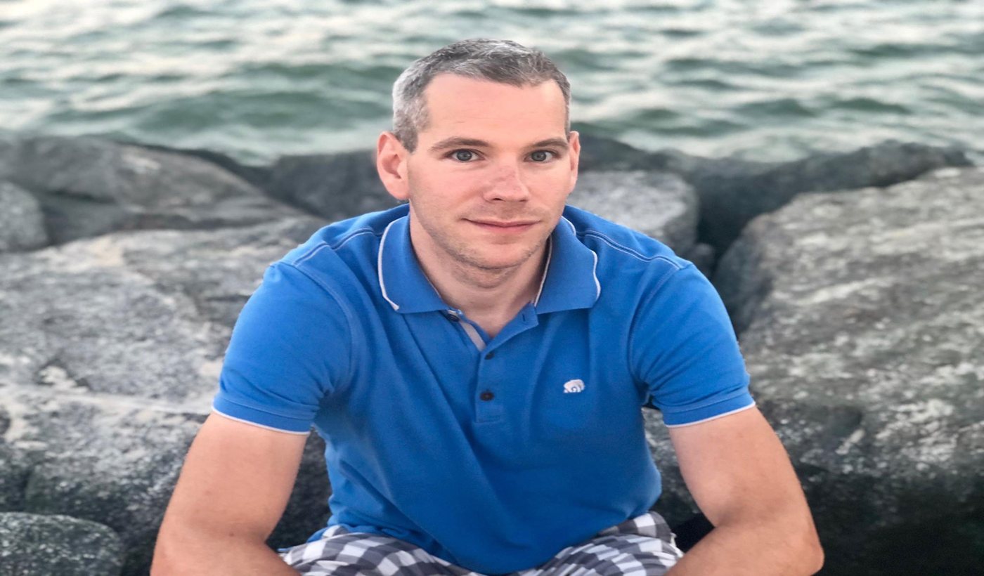 Michael Whyte, founder of Lean Towards Joy, sitting on rocks by the water