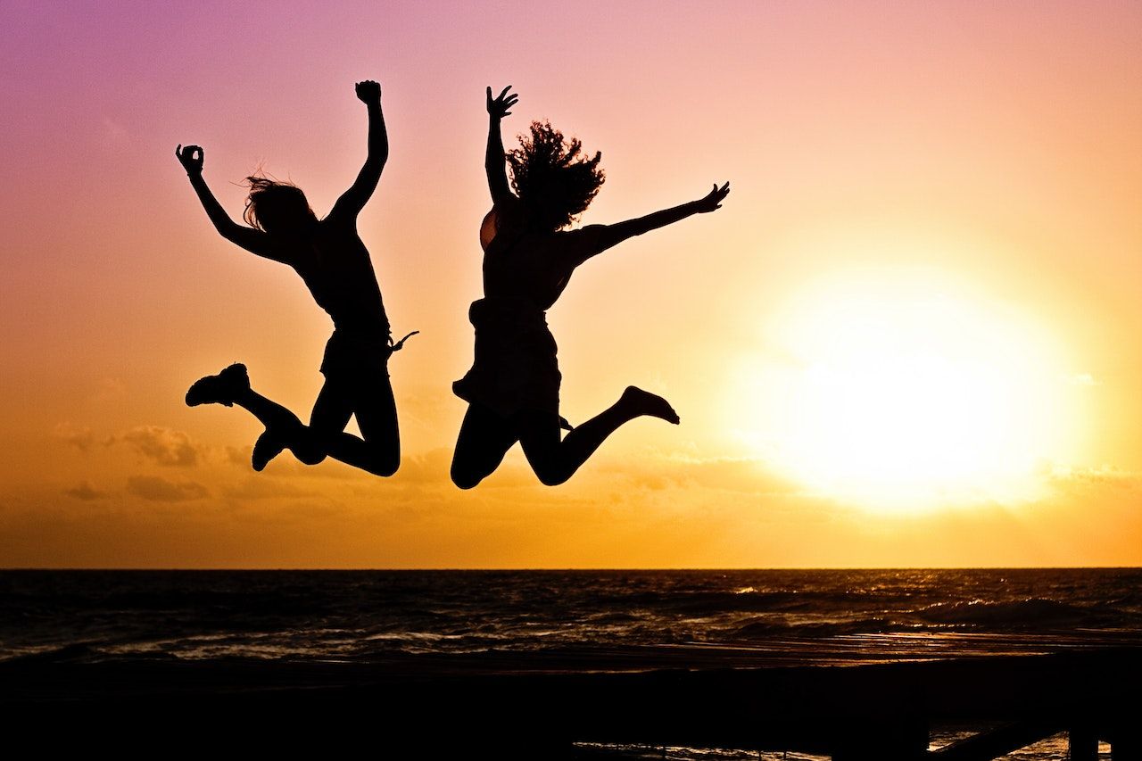 Two friends jumping for joy against an orange sunset
