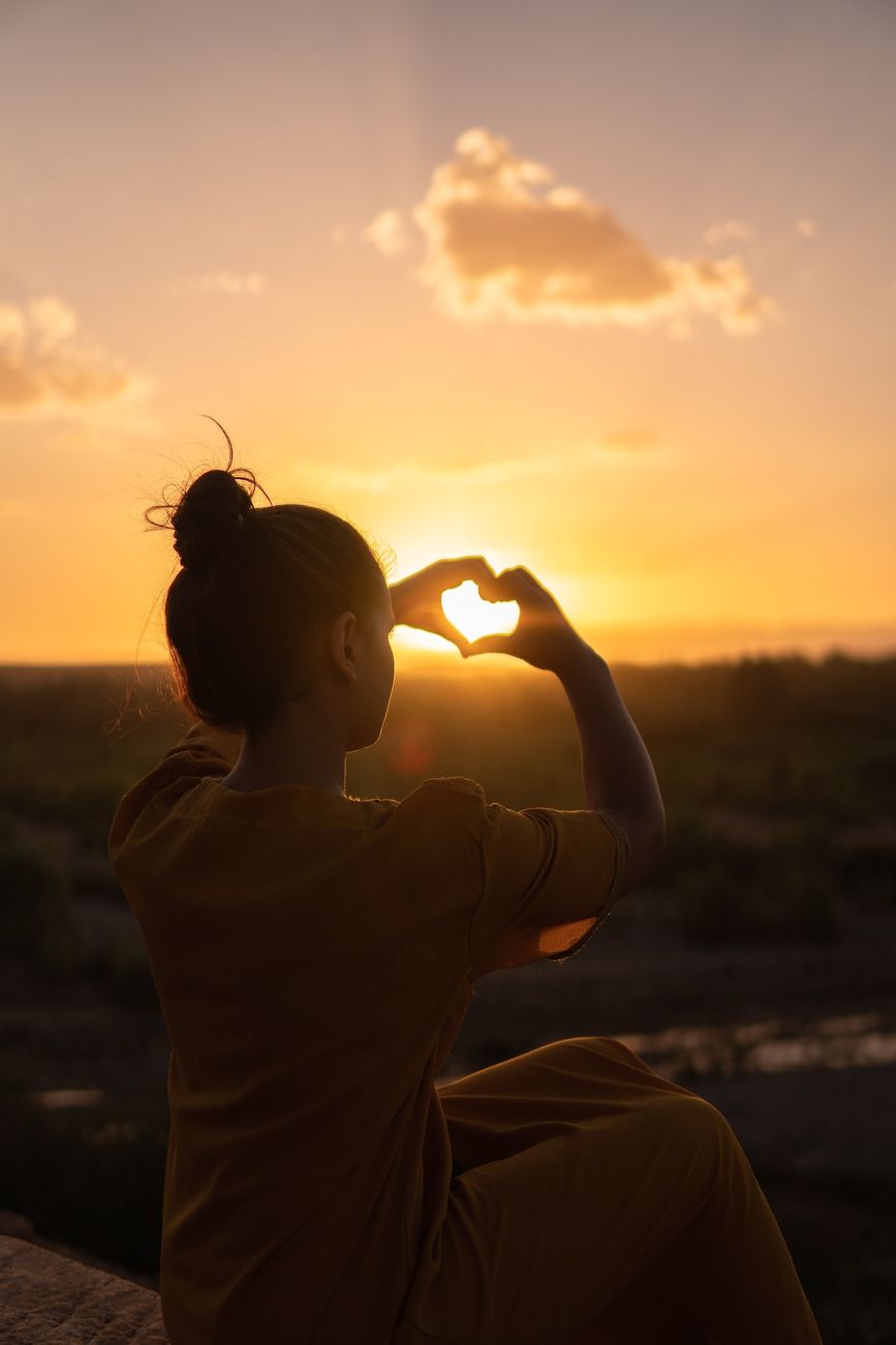 A person making a heart shape with their hands at sunset