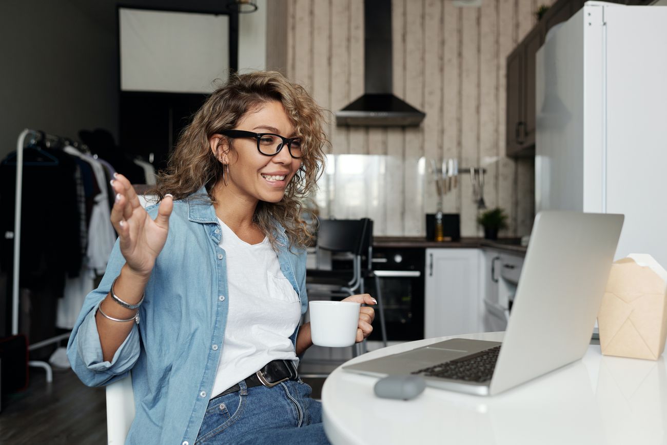 A woman laughing on a video call at her kitchen table